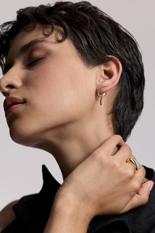 A MODEL LOOKING UPWARD WITH HER EYES CLOSED AND HER HAND LIFTED UP TO CUP HER NECK, AS SHE WEARS A BLACK TOP AND THE MUSE TWIRL STUD EARRINGS