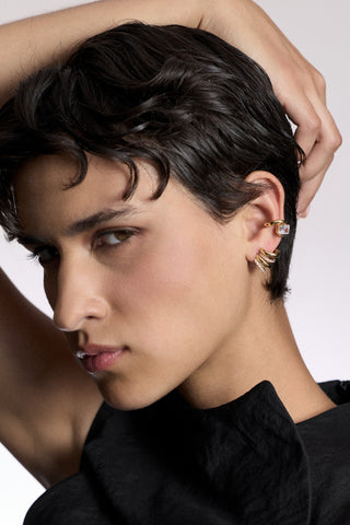 A MODEL LOOKING AT THE CAMERA WITH HER ARM LIFTED AND DRAPED OVER HER HEAD, AS SHE WEARS A BLACK TOP AND THE MUSE MULTI J STUD EARRINGS