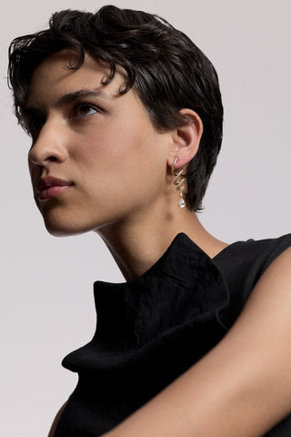 PROFILE OF A MODEL WITH SHORT BLACK HAIR LOOKING OFF TO THE SIDE, WEARING A BLACK TOP AND THE MUSE TWIRL LINEAR DROP EARRINGS