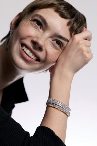A MODEL WITH SHORT RED HAIR LEANING ON HER HAND AS SHE LOOKS UPWARD AND SMILES, WEARING A BLACK TOP AND THE TWINNIE HINGE BRACELETS
