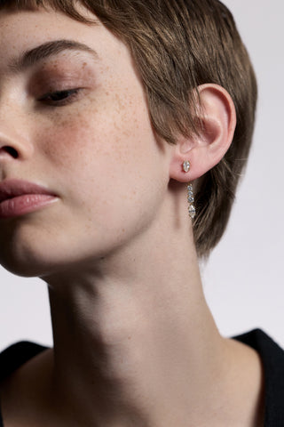 CLOSE UP OF HALF OF A MODEL’S FACE, AS SHE LOOKS DOWN AND WEARS THE TWINNIE FRONTBACK SHORT DROP EARRINGS 