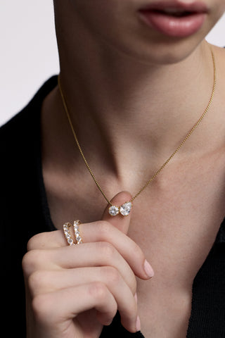 CLOSE UP OF A MODEL’S CHEST AS SHE WEARS A BLACK TOP AND THE TWINNIE TOI MOI PENDANT NECKLACE, WITH HER HAND LIFTED AND HOLDING THE PENDANT IN BETWEEN HER FINGERS