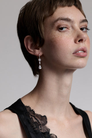 A MODEL TURNED SLIGHTLY TO THE SIDE LOOKING AT THE CAMERA, AS SHE WEARS A BLACK LACE CAMI AND THE TWINNIE LEVERBACK DROP EARRINGS
