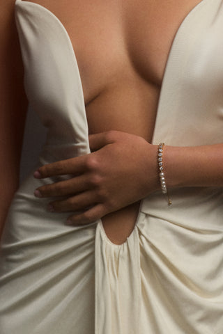 A MODEL’S TORSO IN FRAME, AS SHE WEARS A LOW CUT WHITE DRESS WITH HER HAND ACROSS HER STOMACH, STYLED WITH THE UNDER THE SEA MIXED LINE BRACELET