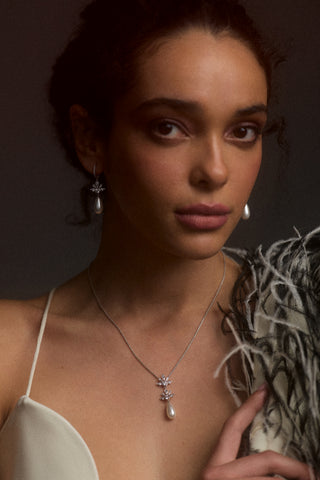 A MODEL LOOKING AT THE CAMERA WEARING A WHITE TOP AND A FEATHER JACKET ON ONE OF HER SHOULDERS, STYLED WITH THE UNDER THE SEA PEARL TEARDROP LEVERBACK EARRINGS AND THE UNDER THE SEA TEARDROP PEARL Y NECKLACE