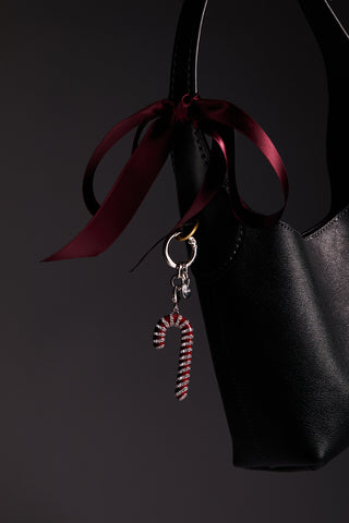 Candy cane-shaped bag charm with pave cubic zirconia accents on a black handbag against a dark background.