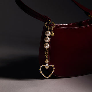 Pearl and heart-shaped charm hanging from a red handbag on a dark background