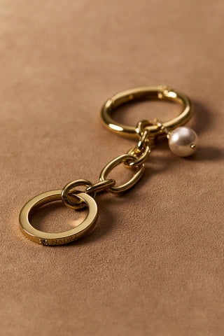 GOLD-TONED BON VOYAGE PEARL CHAIN CHARM 4 AGAINST A BROWN BACKDROP