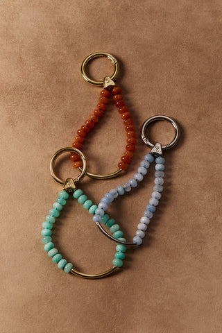 BON VOYAGE AMZ BAG CHARM 4 WITH GOLD-TONED HARDWARE, BON VOYAGE CARN BAG CHARM 4 WITH GOLD-TONED HARDWARE, AND BON VOYAGE BLUE BAG CHARM 3 WITH SILVER-TONED HARDWARE, ALL LAYING AGAINST A BROWN BACKDROP