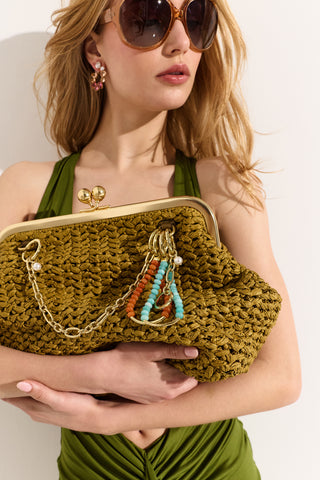 A MODEL WEARING SUNGLASSES AND A GREEN DRESS, HOLDING A GREEN BAG WITH CHARMS ATTACHED TO THE HARDWARE