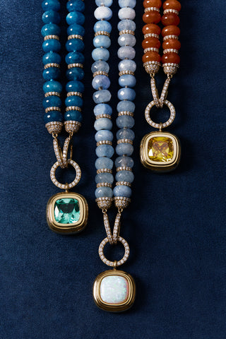 A CLOSE UP OF THE BOUJEE BEADS BLUE LONG NECKLACE, CUSHION DROP LONG NECKLACE, AND CARNELIAN LARGE NECKLACE, LINED UP IN A ROW