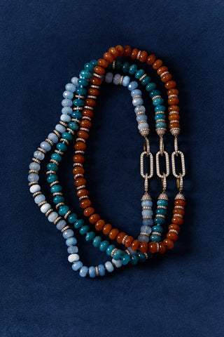 BOUJEE BEADS BLUE BRACELET, CARNELIAN BRACELET, AND LIGHT BLUE BRACELET LAID OUT AGAINST A BLUE BACKGROUND