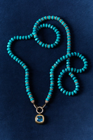 BOUJEE BEADS TURQUOISE LONG NECKLACE LAID OUT AGAINST A BLUE BACKGROUND