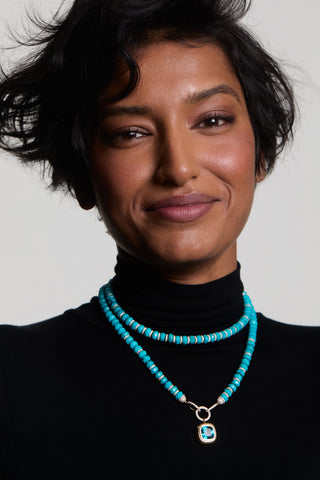 A MODEL IN A BLACK TURTLENECK SMILING AT THE CAMERA WEARING THE BOUJEE BEADS TURQUOISE LONG NECKLACE