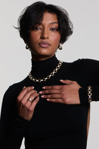 A MODEL WEARING A BLACK TURTLENECK WITH HER HANDS UP TO HER CHEST, WEARING THE EDIE COLLAR NECKLACE, DOOR KNOCKER EARRINGS, LINEAR BRACELET, AND RING