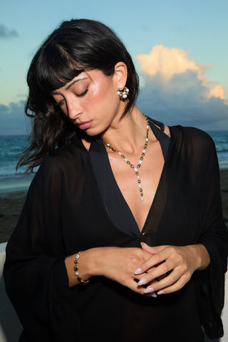 A MODEL ON A BEACH LOOKING AWAY WEARING A BLACK COVER UP, THE PEBBLES FRONTBACK HOOP EARRINGS, LINE BRACELET, AND Y NECKLACE 