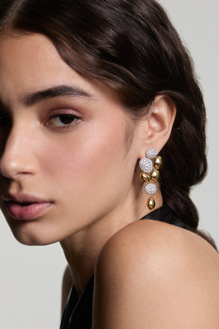 A MODEL LOOKING AT THE CAMERA WITH HALF OF HER FACE IN FRAME, WEARING THE PEBBLES LARGE DROP EARRINGS AND HER HAIR TUCKED BEHIND HER EAR