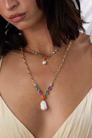 CLOSE UP OF A MODEL’S CHEST WEARING THE FRIEDA MULTI PEARL FRONTAL NECKLACE AND LONG NECKLACE, STYLED WITH A PALE YELLOW TOP