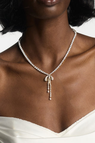 CLOSE UP OF A MODEL’S CHEST WEARING THE EROS BOW TENNIS NECKLACE, STYLED WITH A WHITE GOWN