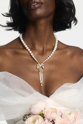 CLOSE UP OF A MODEL’S CHEST WEARING THE EROS BOW PEARL NECKLACE, PAIRED WITH A WHITE DRESS WITH CHIFFON SLEEVES