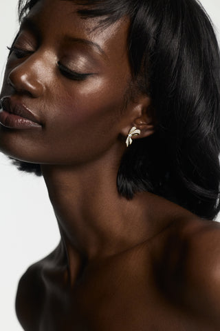 A MODEL WITH BLACK HAIR LOOKING DOWN, WEARING THE EROS SMALL RIBBON STUD EARRINGS