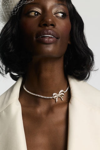 CLOSE UP OF A MODEL WEARING THE EROS BOW CHOKER NECKLACE, STYLED WITH A CREAM JACKET AND LACE HAT