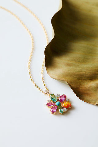FRIEDA FLORAL PENDANT NECKLACE LAID OUT AGAINST A GREEN LEAF 