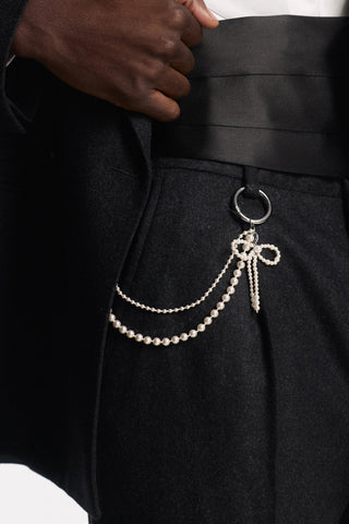 CLOSE UP OF A SUIT PANT WITH THE CEREMONY SWAG BOW LAPEL PIN BAG CHARM CLIPPED ONTO THE BELT LOOP