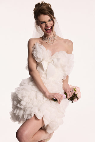 A MODEL WEARING THE PEARL CHOKER ORNATE HIGH NECKLACE AND A LAYERED TULLE WEDDING GOWN, WHILE SHE’S SMILING AND HOLDING A PINK BOUQUET