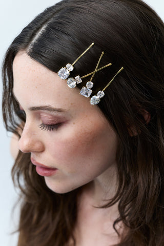 CLOSE UP OF A WOMAN LOOKING DOWN WITH BRUNETTE HAIR, FEATURING FOUR CZ BOBBY PINS OF VARIOUS SHAPES AND SIZES FROM NADRI'S HAIR TODAY COLLECTION PINNED ALONG THE SIDE OF HER HEAD.