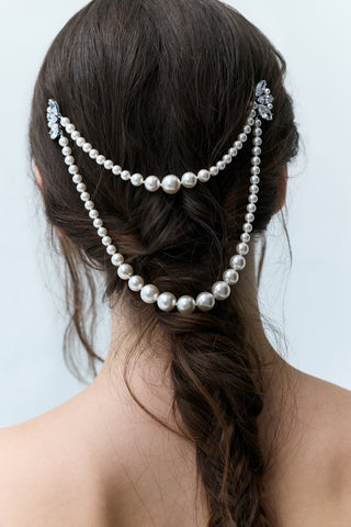 CLOSE-UP OF THE BACK OF A WOMAN’S HEAD WITH A LONG BRUNETTE BRAID FLOWING DOWN HER BACK, FEATURING NADRI’S PEARL SWAG HAIR PIN SECURED NEAR THE TOP OF THE BRAID WITH PEARL STRANDS CASCADING DOWNWARD.