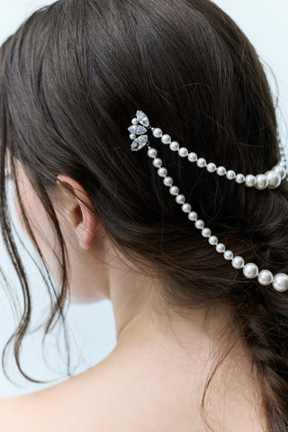 CLOSE-UP OF THE BACK OF A WOMAN’S HEAD WITH A BRUNETTE BRAID, SLIGHTLY TURNED TO THE SIDE TO REVEAL NADRI’S PEARL SWAG HAIR PIN WITH CZ ACCENT PINS ON EACH SIDE.