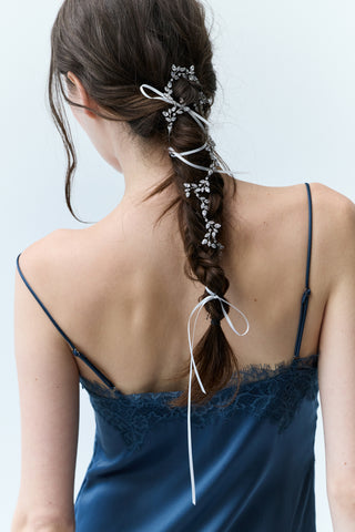 WOMAN IN A BLUE DRESS VIEWED FROM BEHIND, LOOKING SLIGHTLY DOWN WITH A LONG BRUNETTE BRAID FEATURING NADRI’S VINES HAIR GARLAND WOVEN THROUGHOUT.