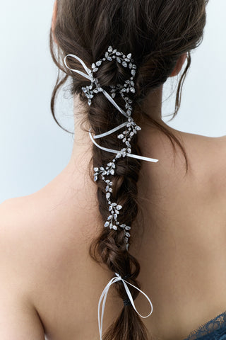 CLOSE-UP OF A WOMAN’S BACK WITH A LONG BRUNETTE BRAID, FEATURING NADRI’S VINES HAIR GARLAND WOVEN THROUGH THE TWISTS AND TURNS OF THE BRAID.