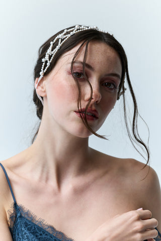 A MODEL LOOKING AT THE CAMERA WITH HER HAIR IN A BRAID BEHIND HER AND HER BANGS FLOWING IN FRONT OF HER FACE, WITH THE PR LATTICE HAIR GARLAND TIED ATOP OF HER HEAD