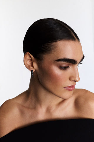 A MODEL LOOKING OFF TO THE SIDE WITH SLICK-BACK HAIR, WEARING A BLACK TOP AND THE TURN UP THE VOLUME BLACK OVAL HOOP EARRINGS