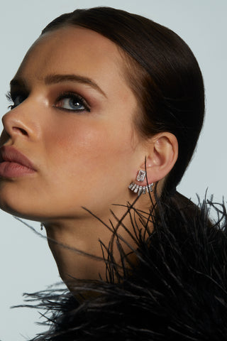 Close-up of a woman wearing earrings with a feathered black garment against a light gray background