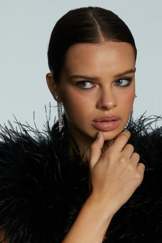 Woman wearing front back linear earrings and a black feathered garment against a light gray background
