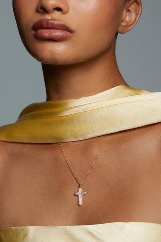 CLOSE UP OF MODEL WEARING CRUSHED CROSS PENDANT NECKLACE. SHE HAS ON A STRAPLESS SILK YELLOW DRESS AND MATCHING SCARF. 