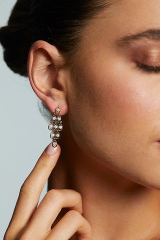 CLOSE UP OF MODEL POINTING TO HER EAR WEARING THE IT GIRL KITE DROP EARRINGS