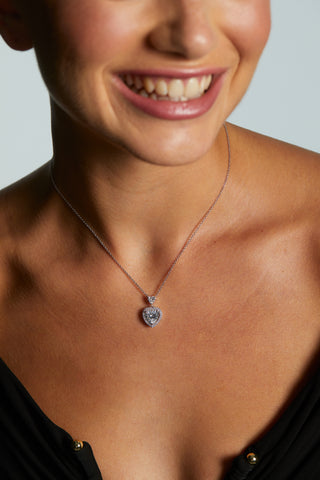 MODEL WEARING LE BISOU HALO HEART NECKLACE WITH A BLACK V NECKLINE DRESS ON WHILE SMILING AND HAIR UP IN A BUN.