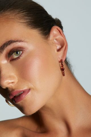 Close-up of a woman's face wearing LE BISOU RED HEART C HOOP EARRINGS with a neutral background