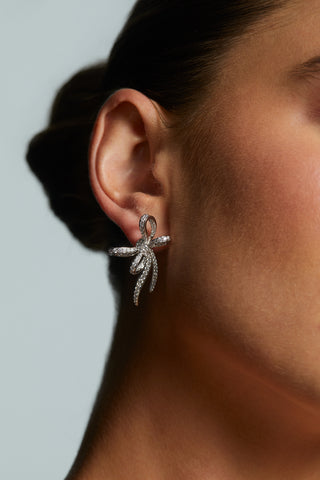 Close-up of a woman wearing LE BISOU PAVE BOW STUD EARRINGS against a neutral background