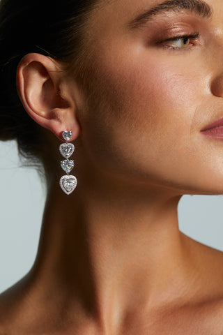 Close-up of a woman wearing LE BISOU HALO HEART LINEAR EARRINGS with a neutral background