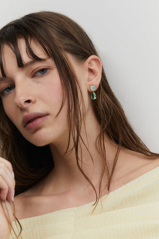A CLOSE UP OF A MODEL WEARING MAIDEN MINT PEAR DROP EARRINGS WITH HER HAIR TUCKED BEHIND HER EAR AND A YELLOW TOP.