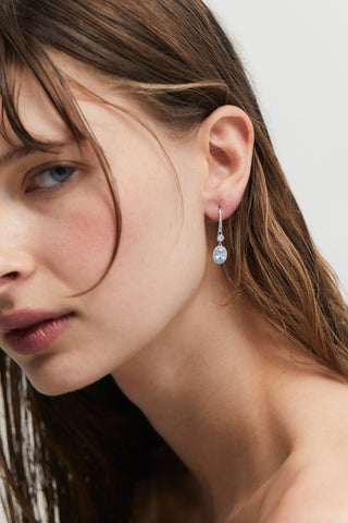 CLOSE UP OF MODEL'S PROFILE WEARING MAIDEN AQUA HALO OVAL LEVERBACK EARRINGS WITH HER HAIR TUCKED BEHIND HER EARS. 