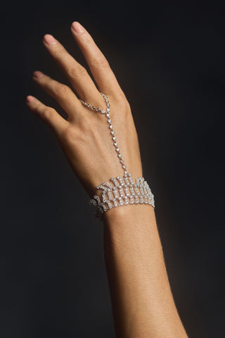 A WOMAN’S HAND LIFTED IN THE AIR AGAINST A BLACK BACKGROUND, WEARING THE FRANCES FRINGE HAND CHAIN BRACELET