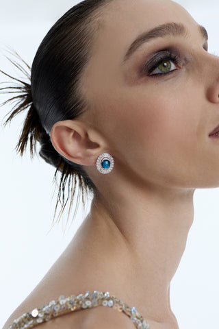 SIDE PROFILE OF A MODEL LOOKING UPWARD AS SHE WEARS HER HAIR IN A SLICK-BACK BUN, A GOLD SPARKLY DRESS, AND THE FRANCES BLUE OVAL BUTTON EARRINGS