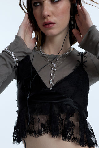 A MODEL LISTENING TO MUSIC WITH HER HANDS ON HER EARPHONES, WEARING A BLACK LACE TOP LAYERED OVER A GRAY SHIRT AND STACKED NECKLACES AND BRACELETS FROM NADRI’S SUPERNOVA COLLECTION