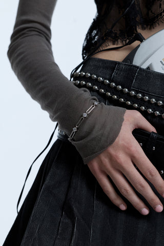 CLOSE-UP OF A MODEL’S HAND RESTING AGAINST HER STATEMENT BELT, WEARING A LACE TOP OVER A GRAY SHIRT AND THE SUPERNOVA LONG LINK BRACELET LAYERED OVER HER SLEEVE